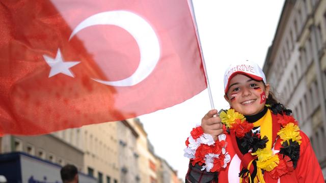 Ein Mädchen trägt zur Fußball-EM eine Blumenkette in schwarz-rot-gold und schwingt die türkische Flagge.