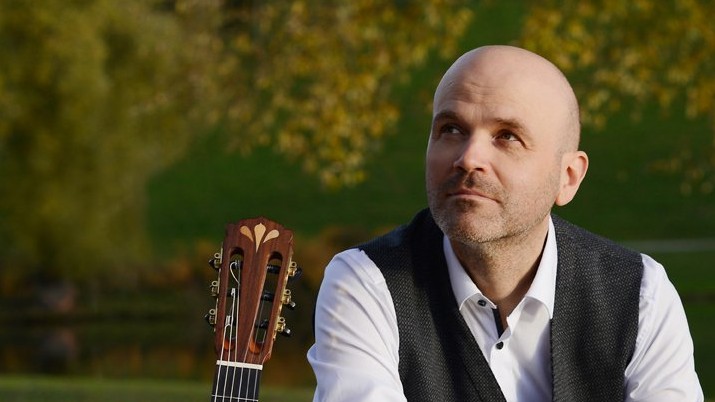 Ein Mann sitzt mit Gitarre in einem Park Ein Mann sitzt mit Gitarre in einem Park