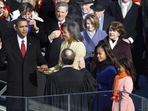 Barack Obama legt die linke Hand auf die Bibel, die seine Frau hält. Die rechte Hand hält er nach oben.