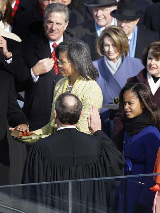 Barack Obama legt die linke Hand auf die Bibel, die seine Frau hält. Die rechte Hand hält er nach oben.