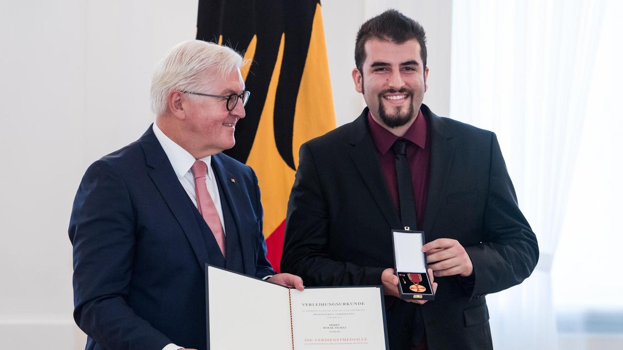 Burak Yilmaz freut sich, weil Bundespräsident Frank-Walter Steinmeier ihm den Verdienstorden der Bundesrepublik Deutschland verleiht. Steinmeyer hält die Urkunde in die Kamera und lächelt milde. Unter dem Motto "Zukunft braucht Erinnerung" würdigt Bundespräsident Steinmeier anlässlich des Tages des Ehrenamtes insgesamt 14 Frauen und 14 Männer für herausragendes Engagement für die Gedenk- und Erinnerungskultur in Deutschland mit dem Verdienstorden. Burak Yilmaz freut sich, weil Bundespräsident Frank-Walter Steinmeier ihm den Verdienstorden der Bundesrepublik Deutschland verleiht. Steinmeyer hält die Urkunde in die Kamera und lächelt milde. Unter dem Motto "Zukunft braucht Erinnerung" würdigt Bundespräsident Steinmeier anlässlich des Tages des Ehrenamtes insgesamt 14 Frauen und 14 Männer für herausragendes Engagement für die Gedenk- und Erinnerungskultur in Deutschland mit dem Verdienstorden.