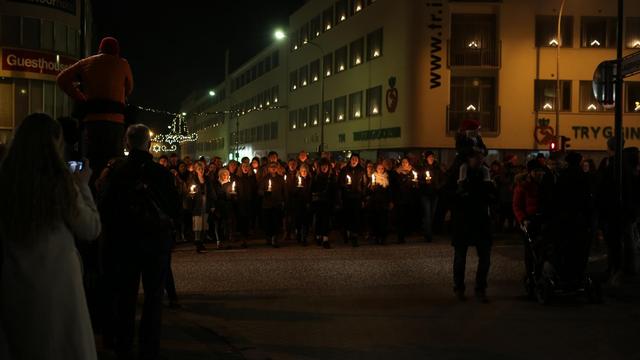 Ein Menschengruppe geht mit einer Kerze in der Hand durch dunkle Straßen.