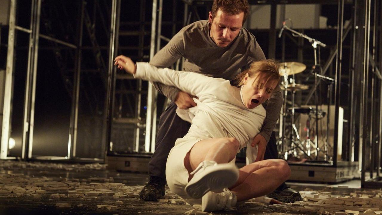Zwei Schaupieler auf einer Bühne. Einer wird von hinten festgehalten, sitzt auf dem Boden. Zwei Schaupieler auf einer Bühne. Einer wird von hinten festgehalten, sitzt auf dem Boden.