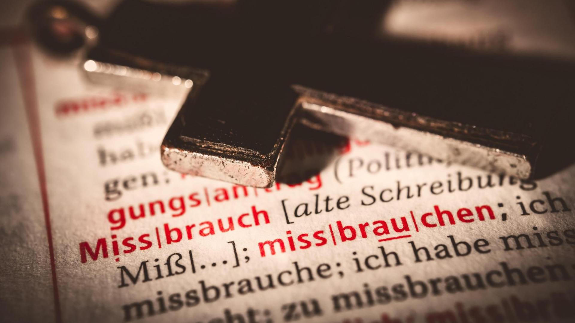Christliches Kreuz auf einem Buch mit Stichwort MISSBRAUCH liegend Christliches Kreuz auf einem Buch mit Stichwort MISSBRAUCH liegend