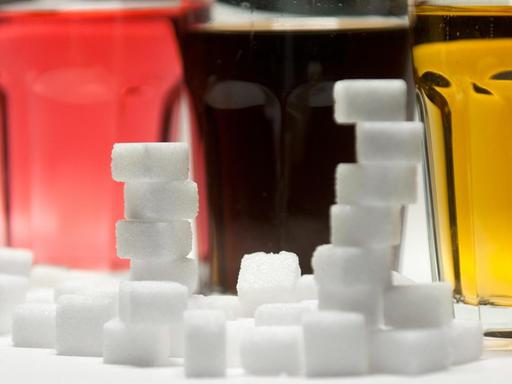 Drei Gläser gefüllt mit roter Limonade, Cola und Energy-Drink stehen am 23.08.2016 in Berlin neben Zuckerwürfeln auf einem Tisch.