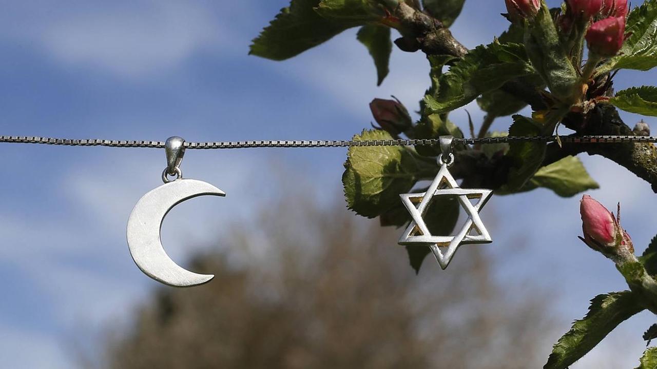 Ein Davidstern und eine Mondsichel hängen als Symbole für Judentum und Islam an einer Kette. Ein Davidstern und eine Mondsichel hängen als Symbole für Judentum und Islam an einer Kette.