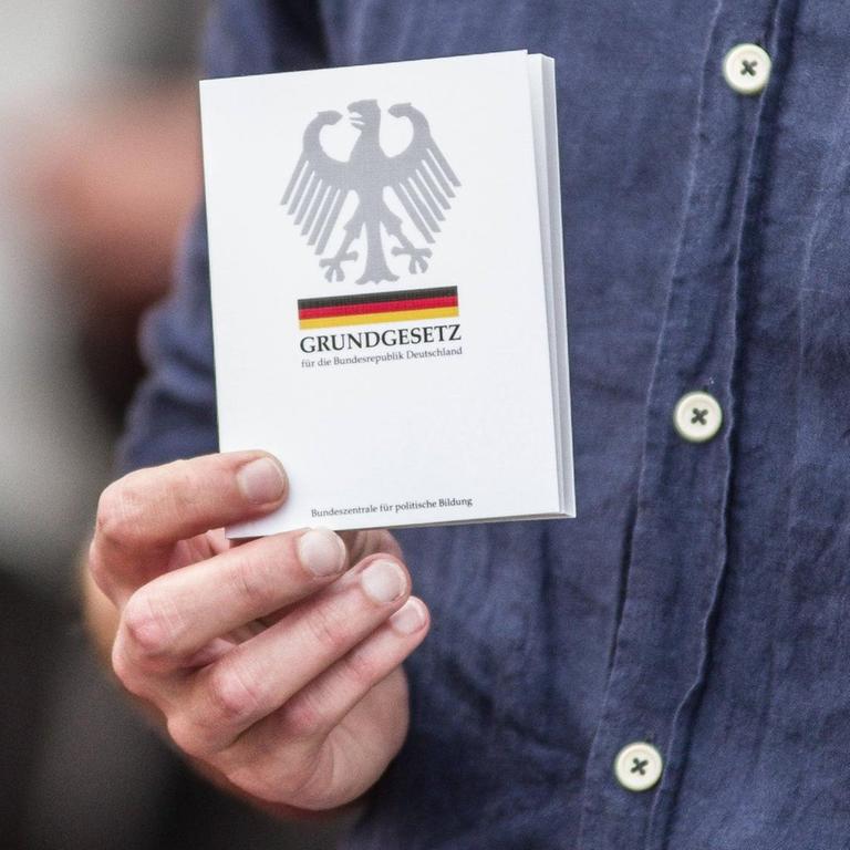 Die Hand eines Mannes hälte eine Ausgabe des deutschen Grundgesetzes. Die Hand eines Mannes hälte eine Ausgabe des deutschen Grundgesetzes.