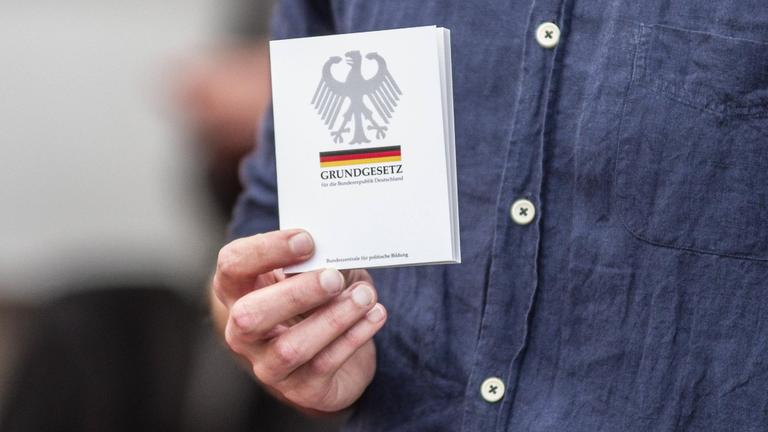 Die Hand eines Mannes hälte eine Ausgabe des deutschen Grundgesetzes.