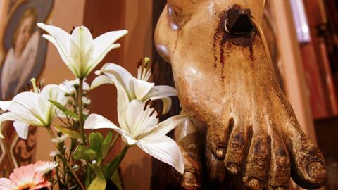 Der Fuß eines Jesus Christus mit dem Detail der Wunde am Fuß ist neben einer frischen Blumenblüte zu sehen.