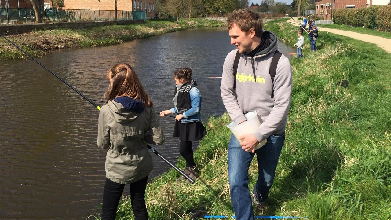 Kilian Neubert, Biologe und Mitarbeiter des Landesanglerverbands, beobachtet am Hagenower Mühlenteich Schülerinnen, die mit einer Angel am Ufer stehen. Kilian Neubert, Biologe und Mitarbeiter des Landesanglerverbands, beobachtet am Hagenower Mühlenteich Schülerinnen, die mit einer Angel am Ufer stehen.