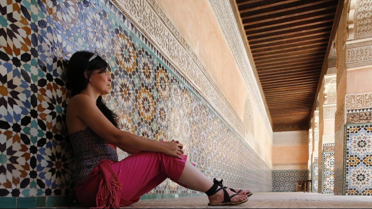 Eine Frau sitzt im Innenhof der Ben Youssef Medersa in Marokko, einer ehemaligen Koran-Schule in Marrakesch