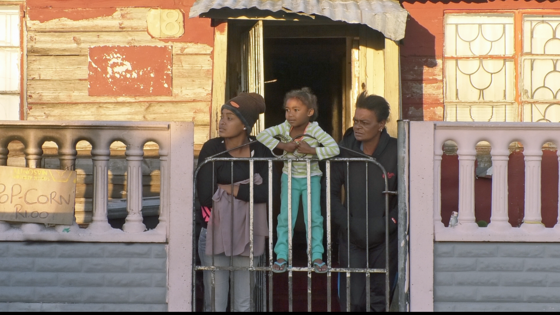 Szene im Stadtteil Manenberg in den Cape Flats von Kapstadt: Zwei Anwohnerinnen mit Kind stehen am Hoftor und schauen die Straße hinunter