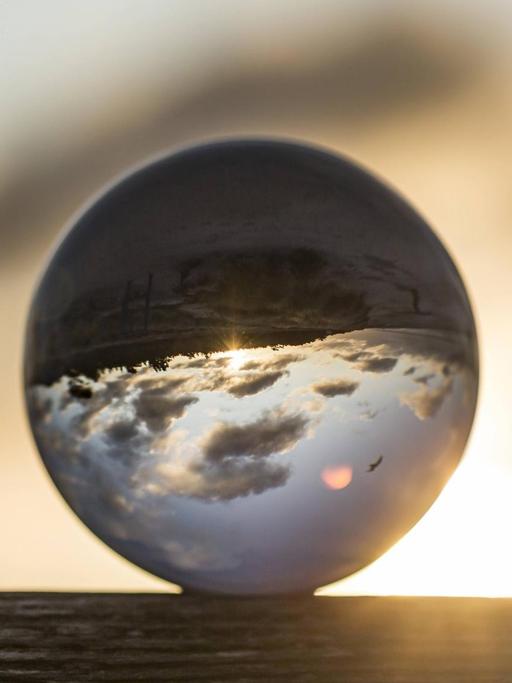 Eine Glaskugel, in der sich der Himmel und Wolken seitenverkehrt spiegeln.