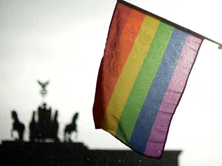 Eine Regenbogenflagge wird in Berlin beim Christopher Street Day (CSD) vor dem Brandenburger Tor gehalten.