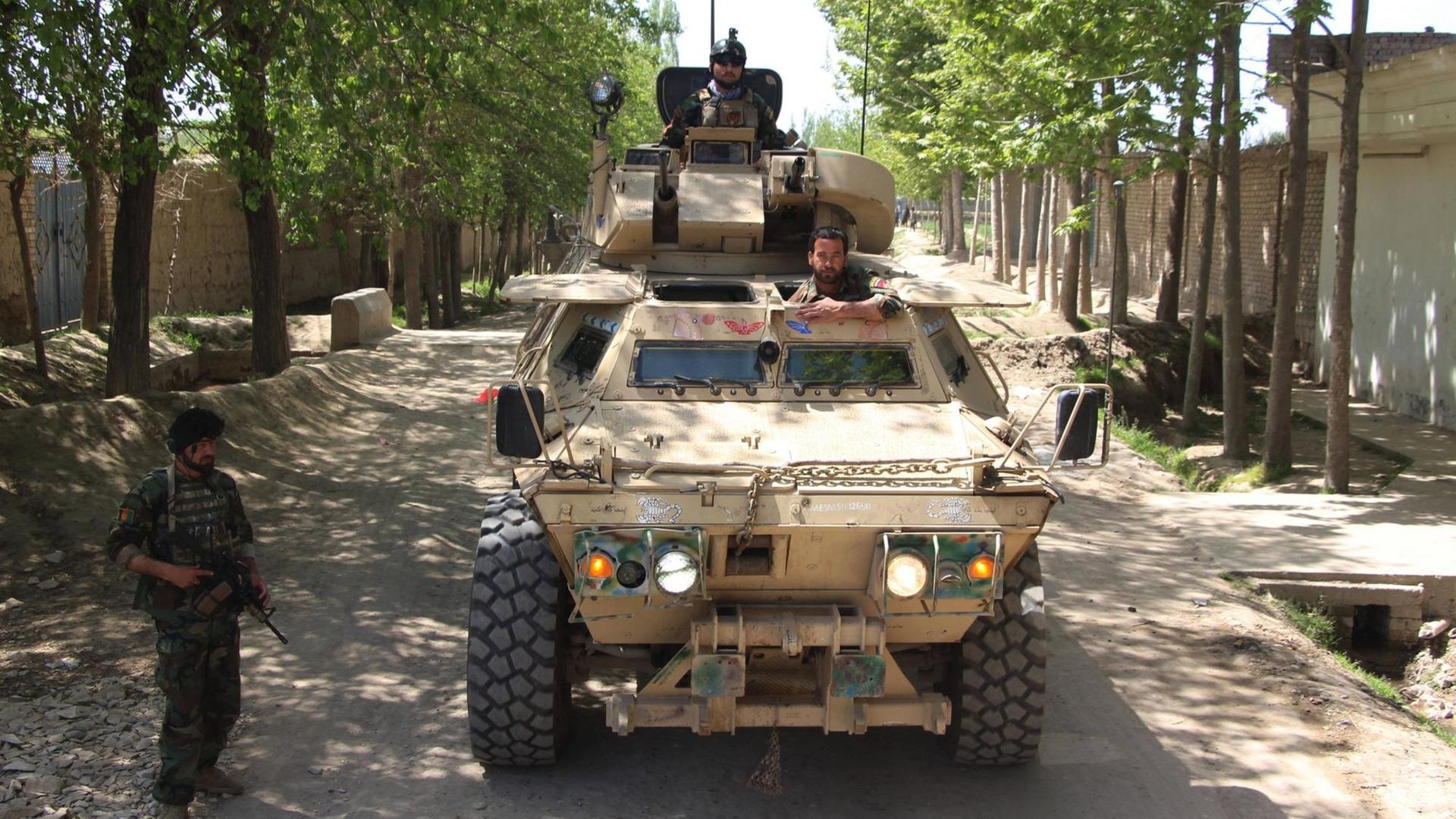 Zwei Männer schauen aus einem Panzer, der auf einer Straße steht. Daneben steht ein weiterer, bewaffneter Mann. Zwei Männer schauen aus einem Panzer, der auf einer Straße steht. Daneben steht ein weiterer, bewaffneter Mann.
