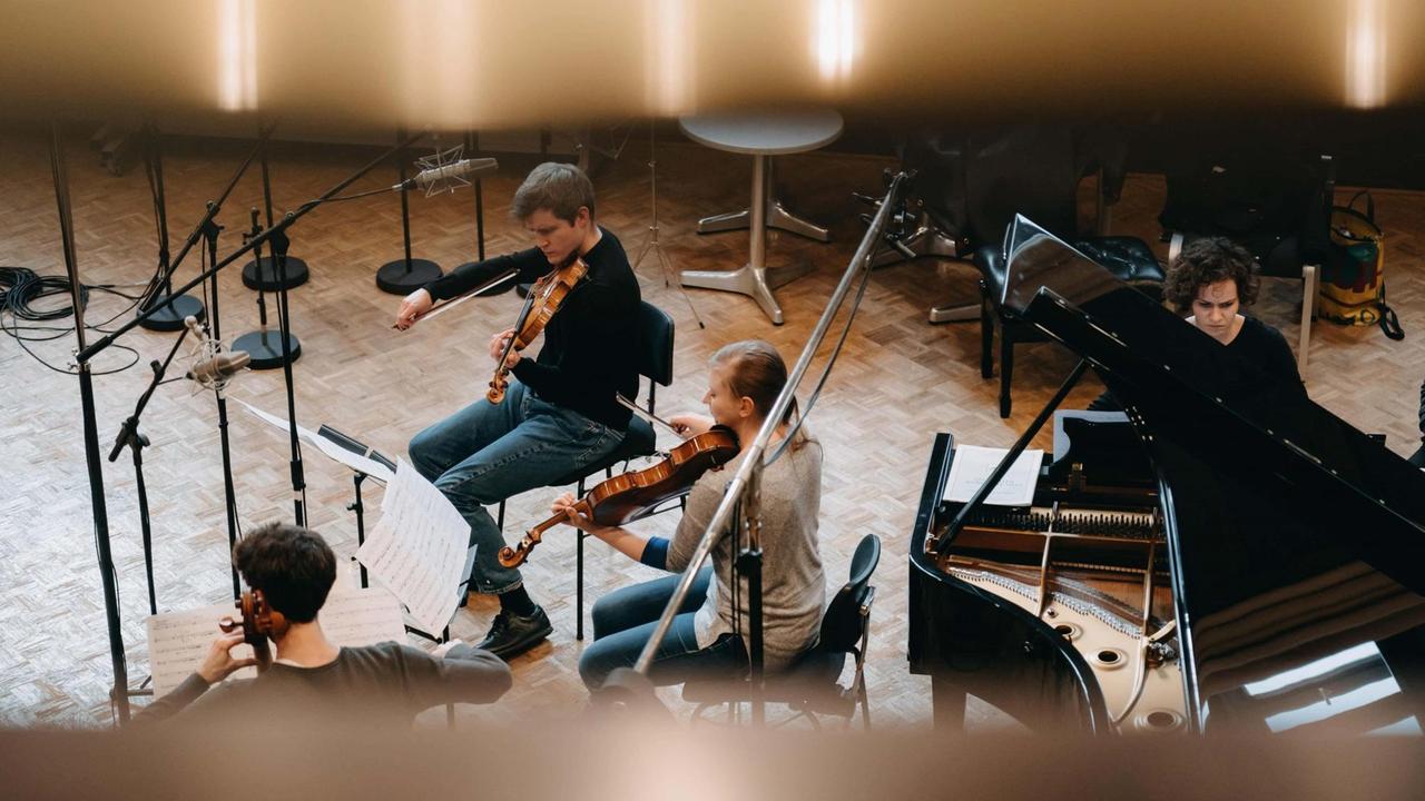 Die Mitglieder des Klavierquartetts sind von einer Galerie aus fotografiert worden, während sie in einem Saal mit Holzparkett musizieren. Die Mitglieder des Klavierquartetts sind von einer Galerie aus fotografiert worden, während sie in einem Saal mit Holzparkett musizieren.
