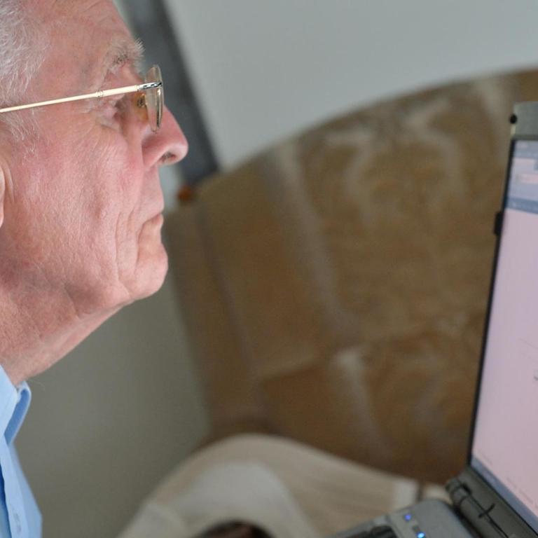 Älterer Herr arbeitet an einem Laptop.