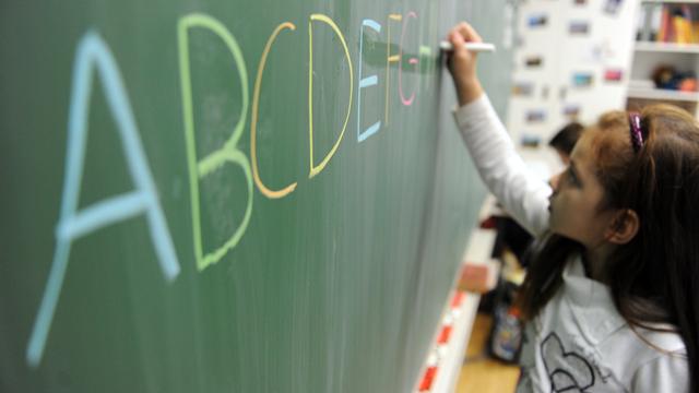 Eine Schülerin schreibt mit bunter Kreide in Großbuchstaben das ABC an eine Tafel.