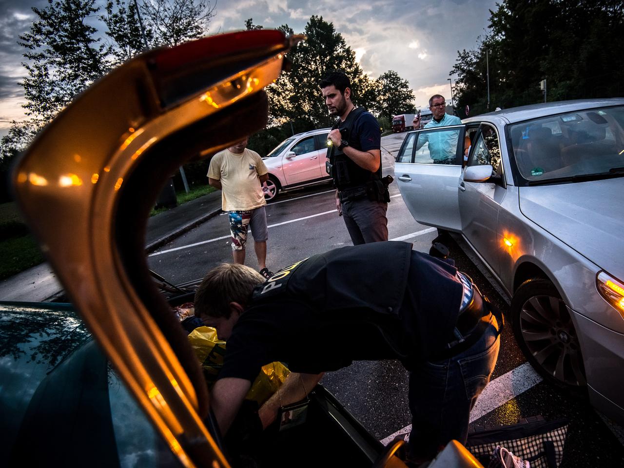 Ein Bundespolizist durchsucht den Kofferraum eines Autos, im Hintergrund stehen mehrere Männer herum. Ein Bundespolizist durchsucht den Kofferraum eines Autos, im Hintergrund stehen mehrere Männer herum.