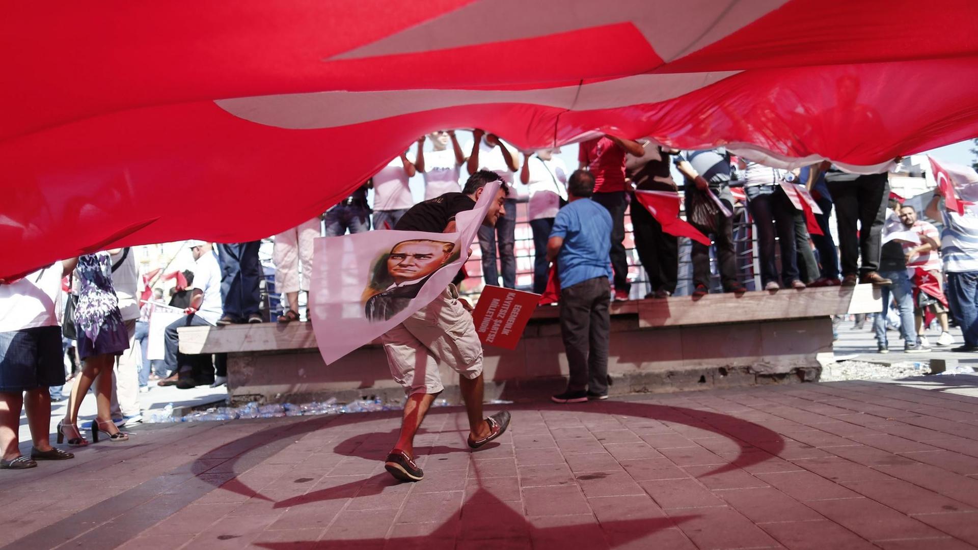 Ein Demonstrant steht unter einer türkischen Flagge und hält eine Fahne mit dem Konterfei von Staatsgründer Atatürk in der Hand. Ein Demonstrant steht unter einer türkischen Flagge und hält eine Fahne mit dem Konterfei von Staatsgründer Atatürk in der Hand.