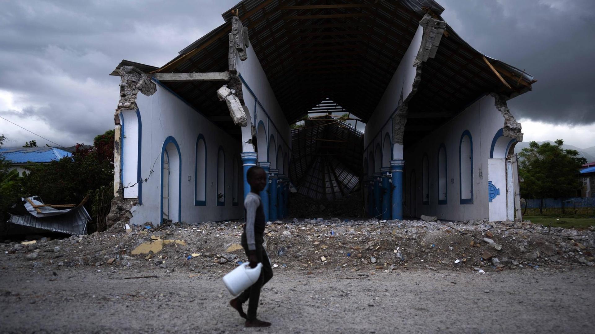 Ein haitianischer Junge läuft mit einer Plastikflasche in der Hand an den Ruinen einer zerstörten Kirche vorbei.
