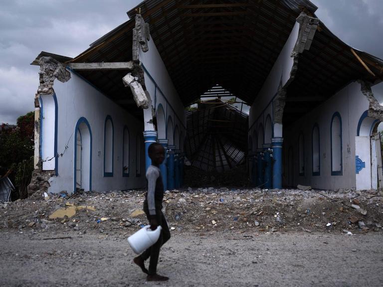 Ein haitianischer Junge läuft mit einer Plastikflasche in der Hand an den Ruinen einer zerstörten Kirche vorbei.