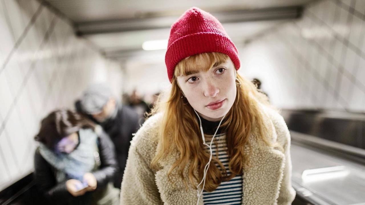 Ein Mädchen fährt leicht verträumt mit ihren Kopfhörer im Ohr auf einer Rolltreppe zur nächsten U-Bahnstation in Köln.