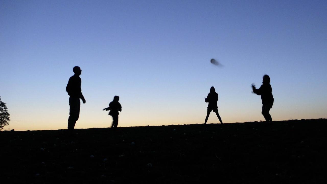 Vier Personen spielen Ball vor einem rot-blauen Himmel.