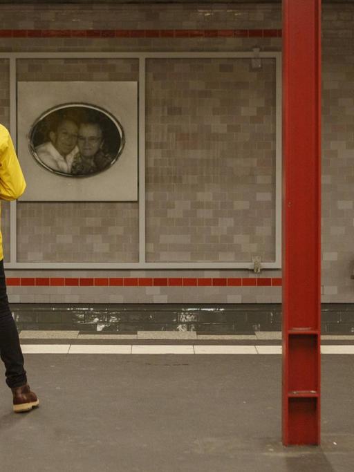 Ein Fahrgast in gelber Jacke steht alleine auf dem verlassenen Bahnsteig. Er steht mit dem Rücken zur Kamera und wartet auf einen Zug.
