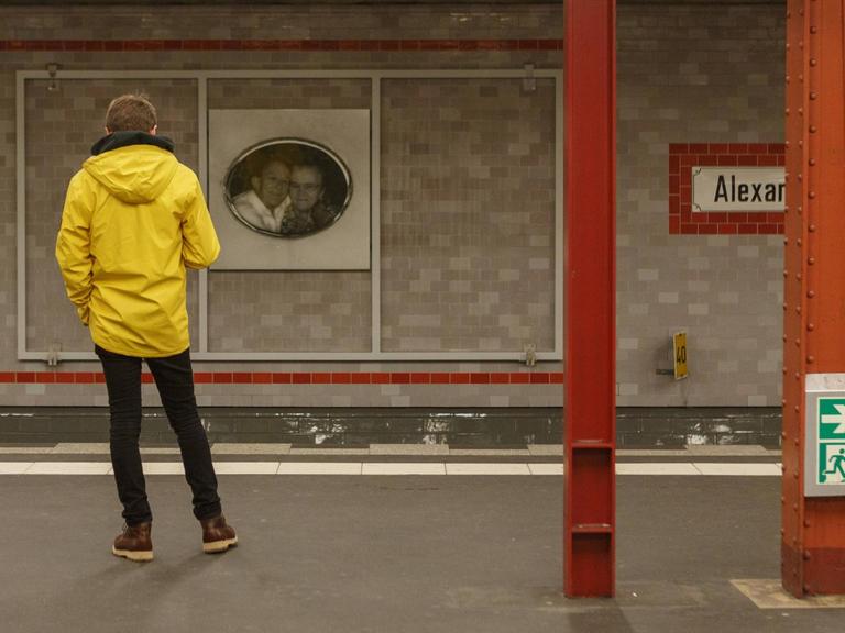 Ein Fahrgast in gelber Jacke steht alleine auf dem verlassenen Bahnsteig. Er steht mit dem Rücken zur Kamera und wartet auf einen Zug.