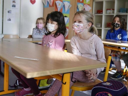 Grundschülerinnen sitzen mit Mund-Nasen-Schutz in einem Klassenraum in Düsseldorf, vor ihnen liegen die Corona-Teststäbchen für den sogenannten Lolli-Test