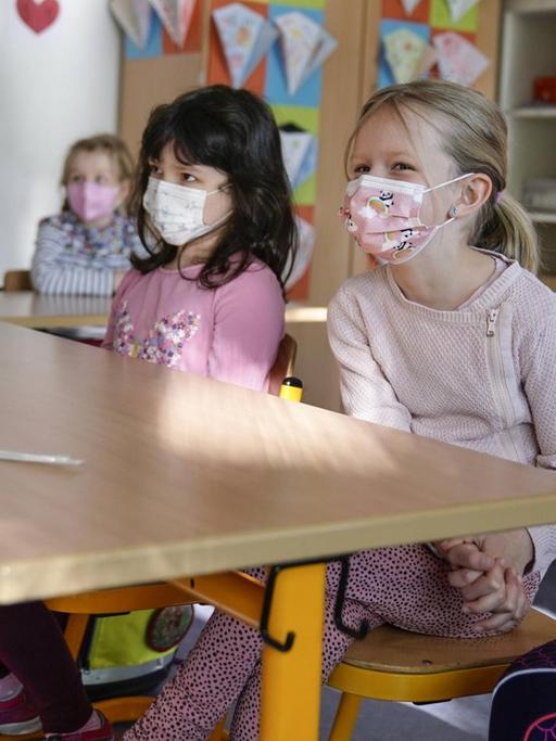 Grundschülerinnen sitzen mit Mund-Nasen-Schutz in einem Klassenraum in Düsseldorf, vor ihnen liegen die Corona-Teststäbchen für den sogenannten Lolli-Test