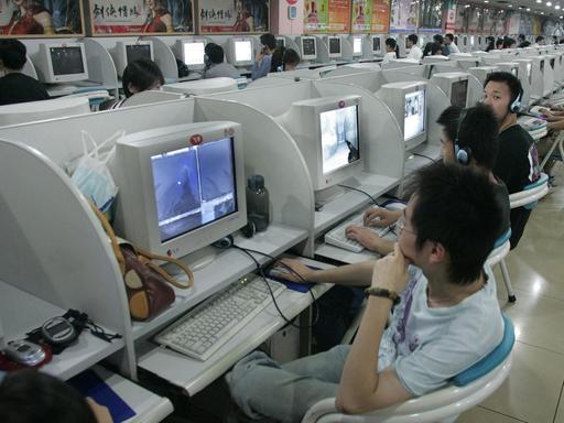 Blick in ein chinesisches Internetcafé: In einer Halle sind in langen Reihen Plätze mit Computern aufgebaut. Junge Menschen sitzen an den Rechnern.