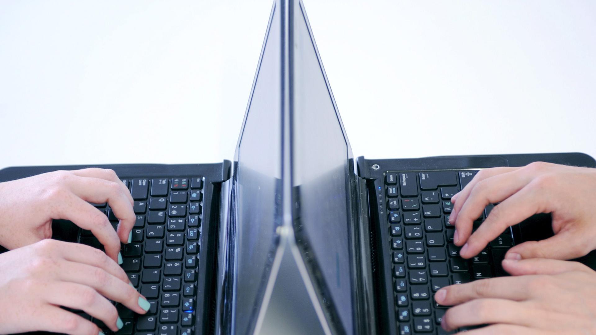 Zwei Laptops stehen sich gegenüber. Hände tippen darauf. Zwei Laptops stehen sich gegenüber. Hände tippen darauf.