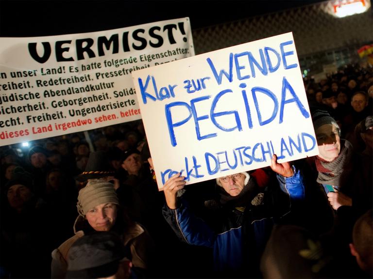 Teilnehmer einer Kundgebung der Pegida in Dresden (Sachsen) halten am 08.12.2014 Transparente in die Höhe.