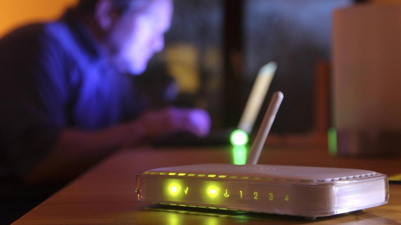 Computer Nutzer in einer Wohnung, im Vordergrund steht ein WLAN-Router. Computer Nutzer in einer Wohnung, im Vordergrund steht ein WLAN-Router.