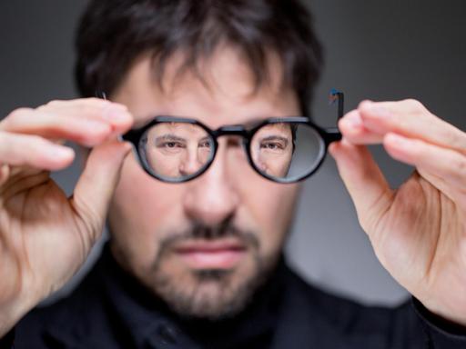 Der italienische Komponist Francesco Filidei hebt seine Brille vor sein Gesicht und spiegelt sich darin