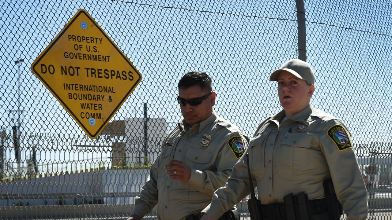 Sicherheitskräfte in Uniform gehen an einem Stacheldrahtzaun entlang. Daran hängt ein gelbes Schild mit schwarzer Aufschrift, wonach der Grenzübertritt verboten ist.