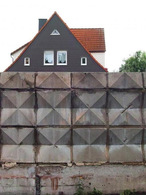 Das Foto zeigt ein Hause mit Spitzdach hinter einer Mauer aus verzierten Steinelementen an der ehemaligen DDR-Grenze im Eckertal zwischen Bad Harzburg und Stapelburg, 32 Jahre nach dem Mauerfall.