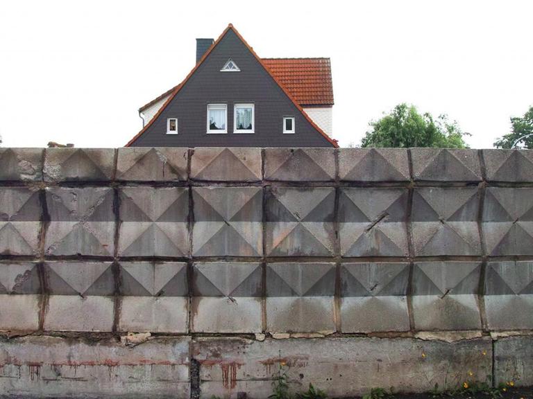 Das Foto zeigt ein Hause mit Spitzdach hinter einer Mauer aus verzierten Steinelementen an der ehemaligen DDR-Grenze im Eckertal zwischen Bad Harzburg und Stapelburg, 32 Jahre nach dem Mauerfall.