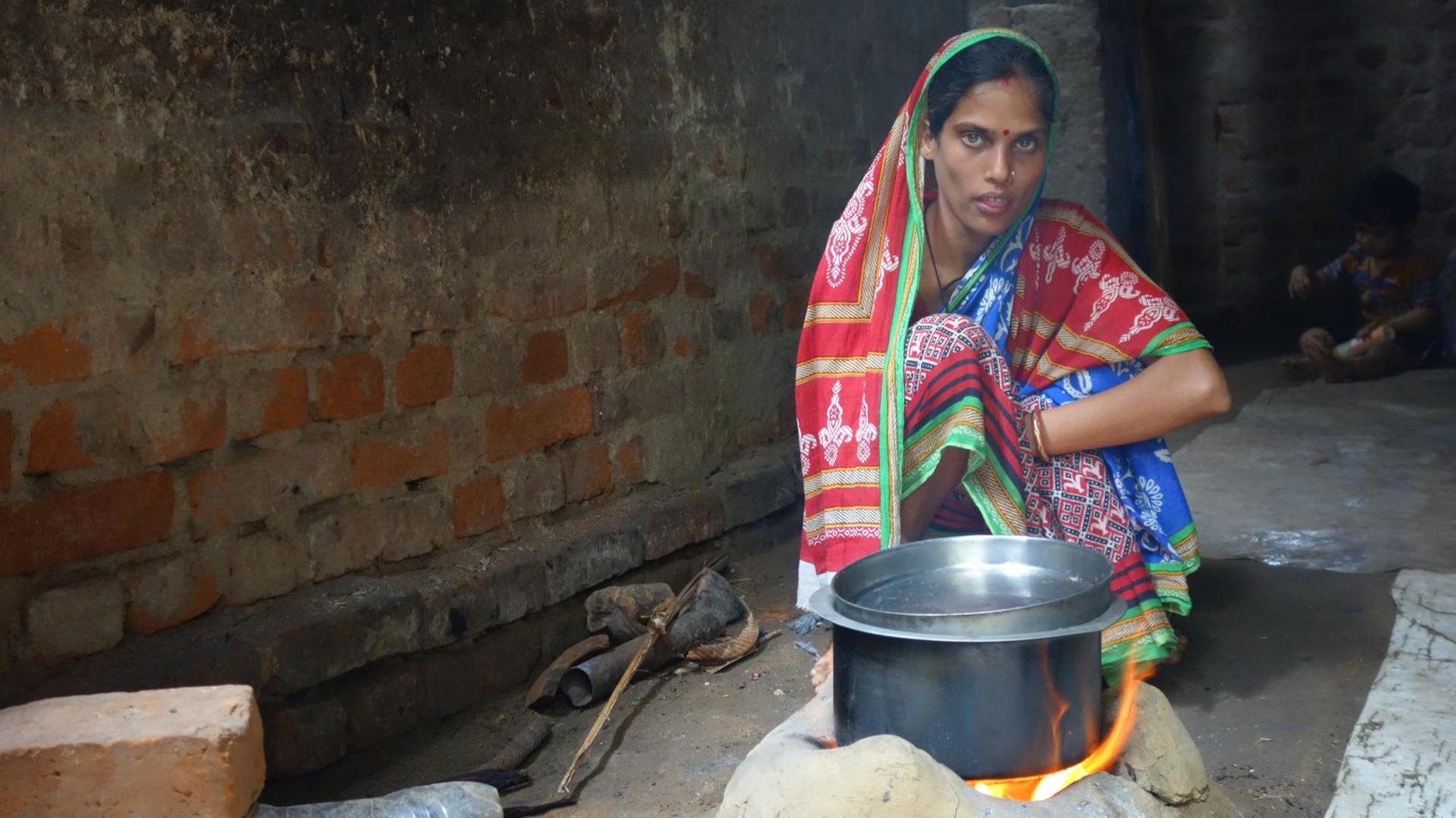 In den Dörfern des ärmsten indischen Bundesstaates Odisha kochen viele Familien auf offenem Feuer im Wohnhaus. Hier sitzt eine Frau am Kochtopf auf dem Boden, dahinter ein Kind. In den Dörfern des ärmsten indischen Bundesstaates Odisha kochen viele Familien auf offenem Feuer im Wohnhaus. Hier sitzt eine Frau am Kochtopf auf dem Boden, dahinter ein Kind.