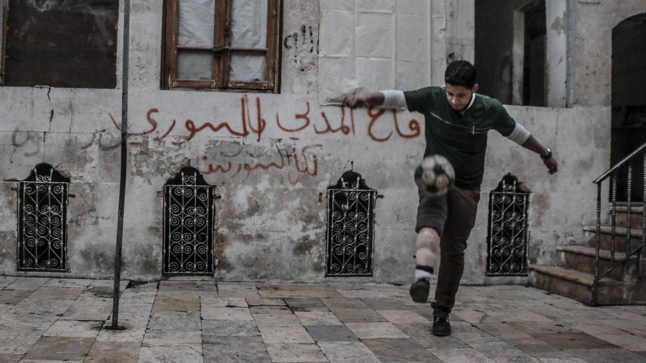 Eine Straßenszene zeigt einen jungen Mann beim Fußball spielen in einem von Rebellen kontrollierten Gebiet in Aleppo 2015. Der Spieler verlor ein Bein nach einem Bombenangriff von Truppen des syrischen Präsidenten Bashar al-Assad.