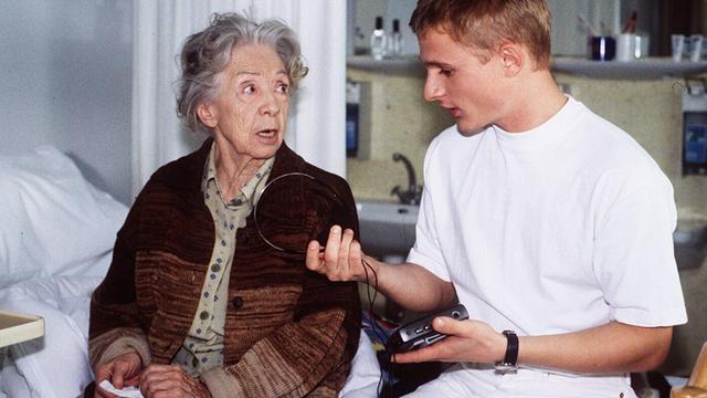 Standbild aus einem ARD-Film, indem Inge Meysel als Oma und Florian Lukas als junger Mann mit einem Walkman am Krankenhausbett sitzen. Oma schaut mit erschreckten Augen auf den jungen Mann, der ihr sein Gerät erklärt.