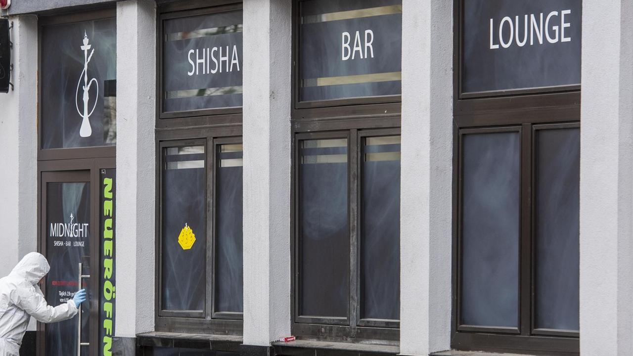 Ein Polizist in weißer Schutz-Kleidung betritt das Lokal. Über dem Eingang steht "Shisha Bar Lounge". Ein Polizist in weißer Schutz-Kleidung betritt das Lokal. Über dem Eingang steht "Shisha Bar Lounge".