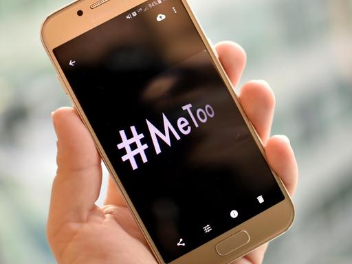 Eine junge Frau hält ein Smartphone mit dem Hashtag "#MeToo" in der Hand