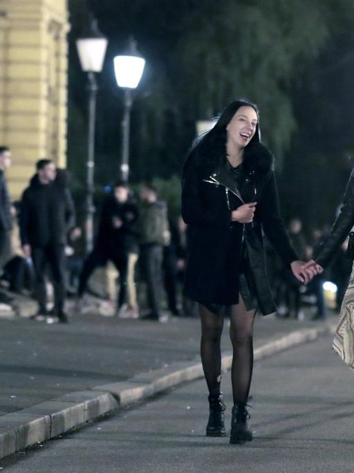 Zwei Mädchen laufen lachend und Händchen haltend einen Weg entlang, im Hintergrund stehen weitere Jugendliche.