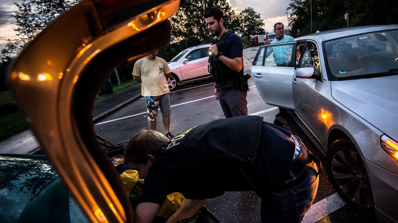 Ein Bundespolizist durchsucht den Kofferraum eines Autos, im Hintergrund stehen mehrere Männer herum. Ein Bundespolizist durchsucht den Kofferraum eines Autos, im Hintergrund stehen mehrere Männer herum.