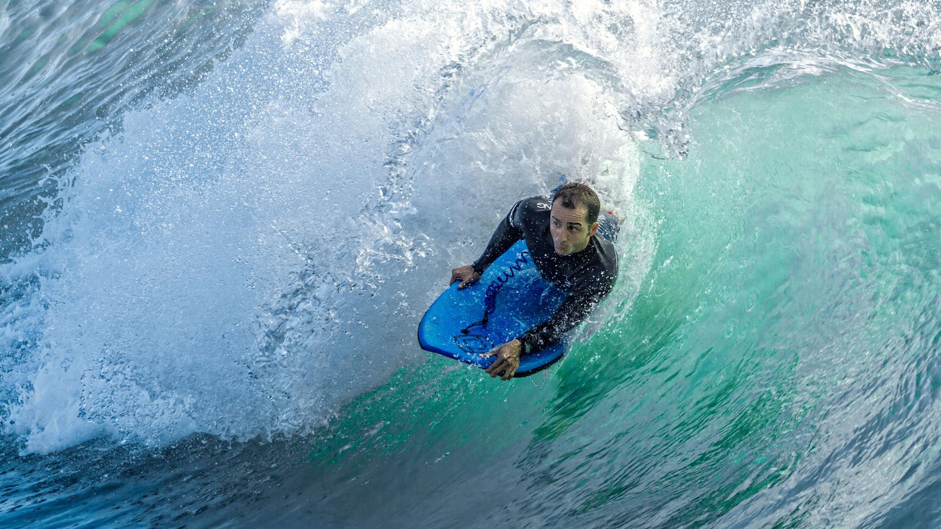 Ein Surfer liegt auf seinem Brett, während er durch eine große Welle gleitet.