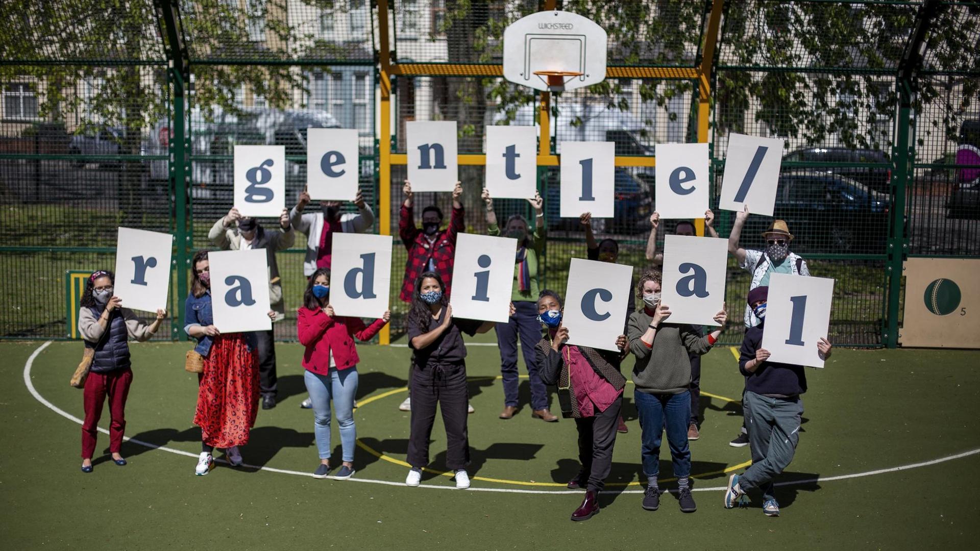 14 Mitglieder des Kunstkollektivs "Gentle/Radical" halten Schilder mit Buchstaben hoch - zusammen ergeben sie den Namen des Kollektivs. 14 Mitglieder des Kunstkollektivs "Gentle/Radical" halten Schilder mit Buchstaben hoch - zusammen ergeben sie den Namen des Kollektivs.
