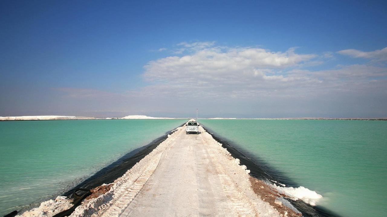 Ein Wagen fährt über eine Straße durch einen Salzsee in der Atacama-Wüste. Ein Wagen fährt über eine Straße durch einen Salzsee in der Atacama-Wüste.